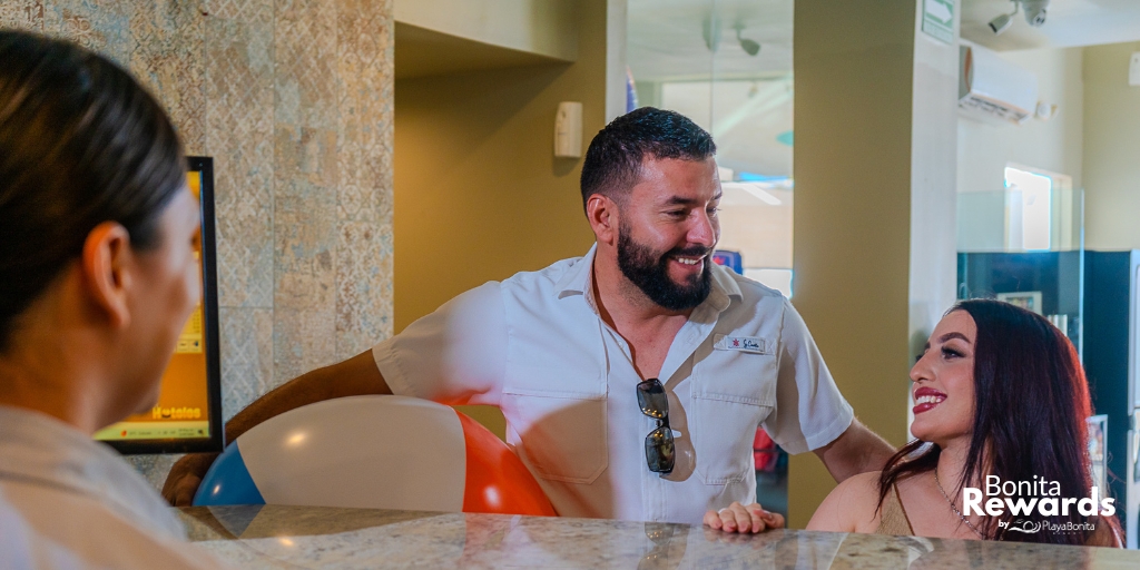 A couple smiling at the Playa Bonita Resort front desk during check-in, representing the personalized experience of the Bonita Rewards loyalty program.